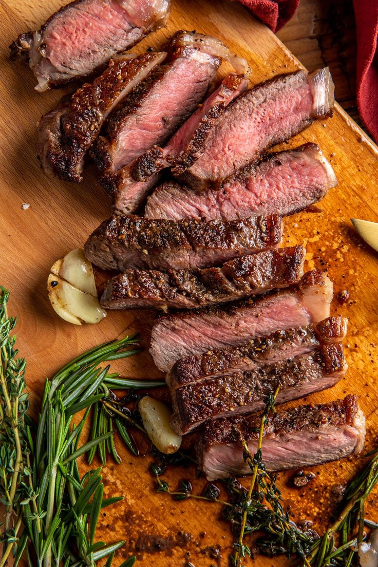 steak sliced up on a cutting board with herbs and seasoning next to the meat