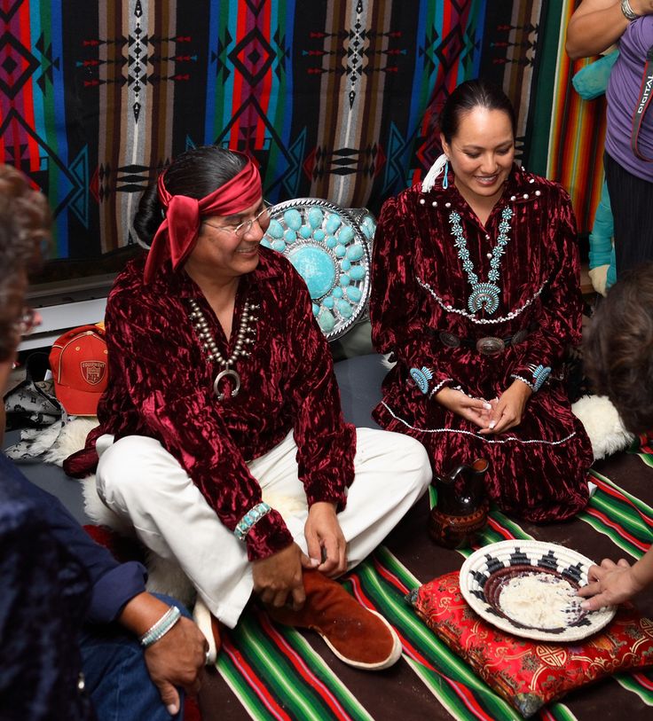 two women sitting on the ground in front of a cake and other people standing around