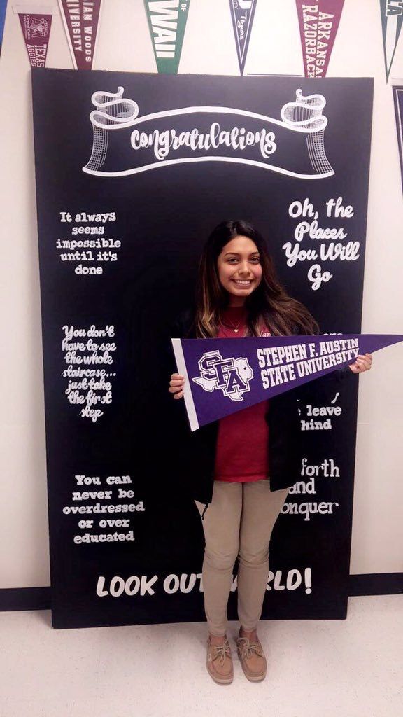 a girl holding a purple and white flag in front of a blackboard with congratulations written on it