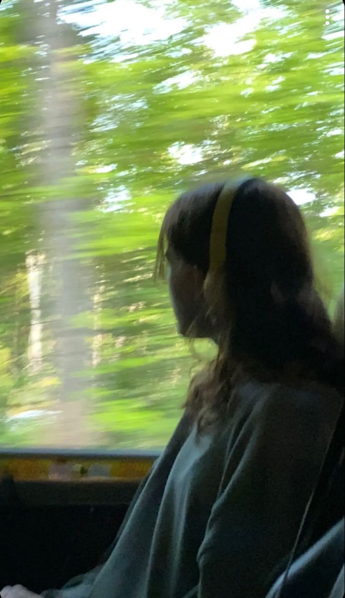 a woman sitting in the passenger seat of a bus looking out the window at trees