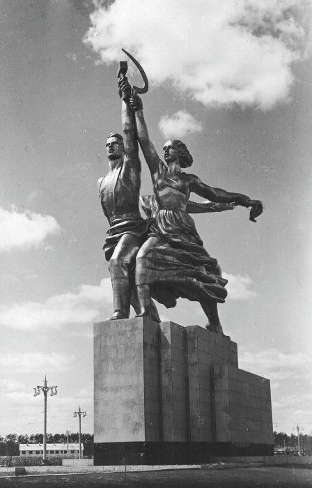 a statue of two women holding an ax in front of a sky background with clouds