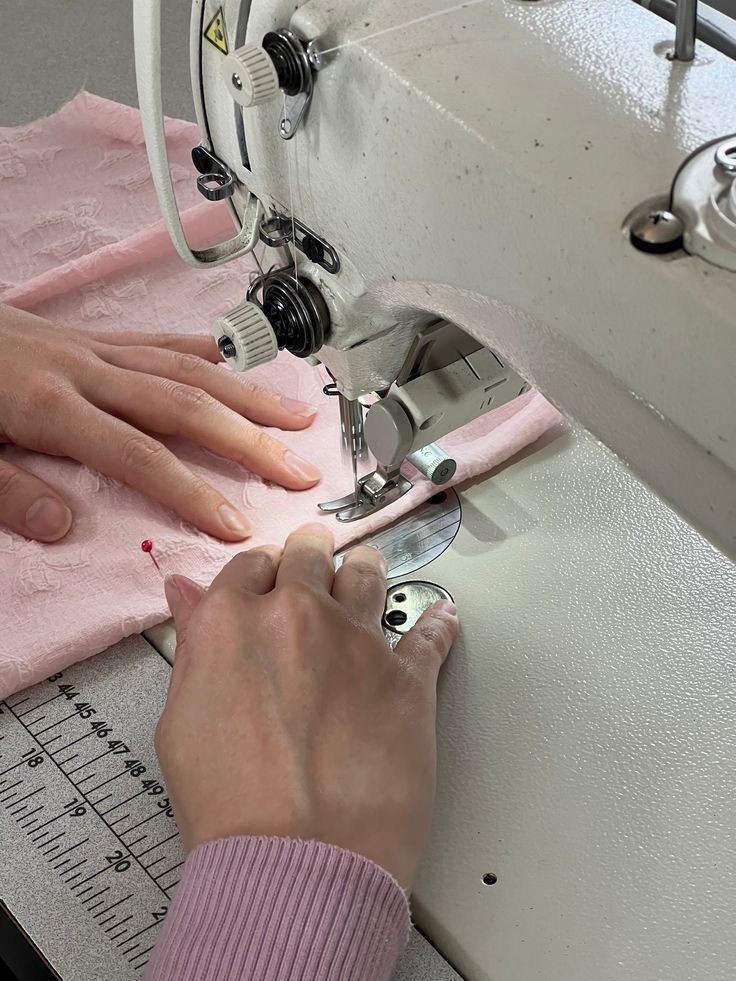 a woman is using a sewing machine to sew on pink fabric with her hands