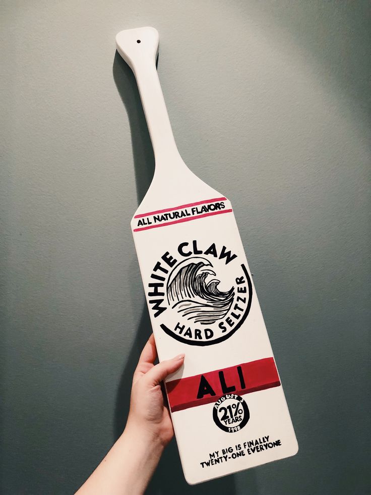 a hand holding a white claw paddle with an all natural flavor logo on the side