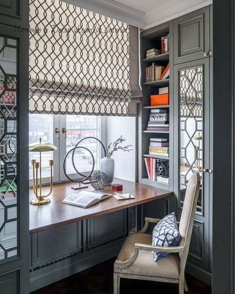 a desk with a chair, lamp and bookshelf in front of the window