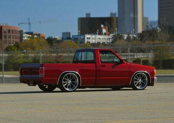 a red pick up truck parked in a parking lot next to a cityscape