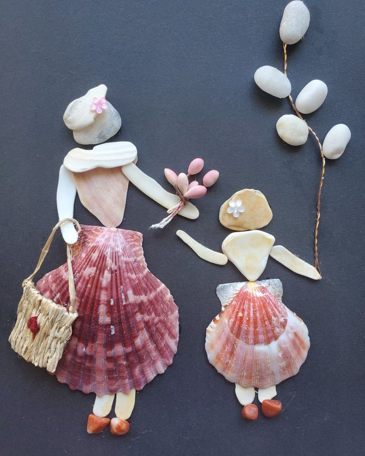 two dolls made out of seashells and shells on a black surface, one holding a basket