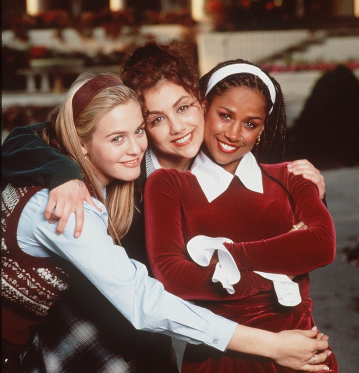 three young women hugging each other and smiling at the camera, with one woman wearing a red velvet dress