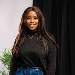 a woman standing in front of a black backdrop wearing jeans and a turtle neck sweater