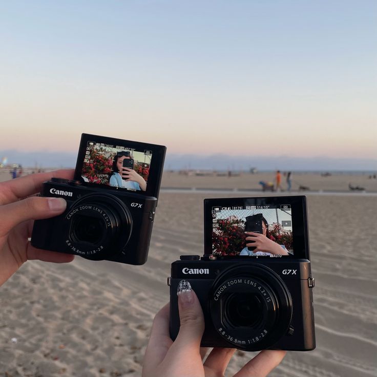 two people holding up their cameras on the beach