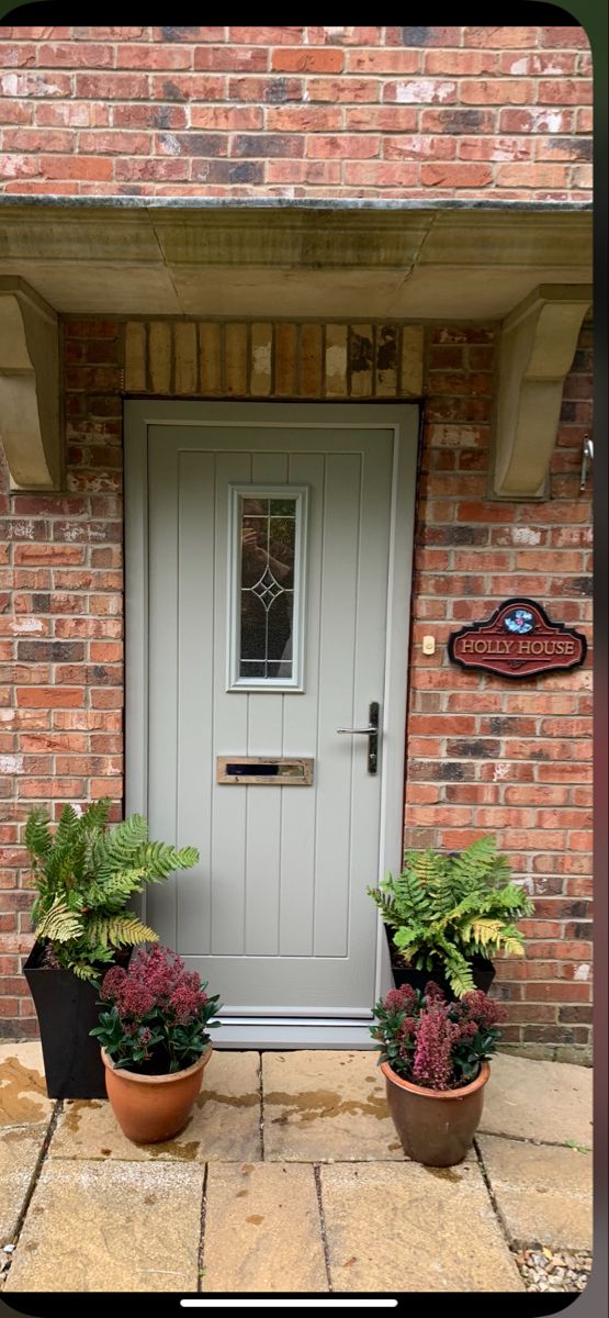 two potted plants sit outside the front door of a brick building with a welcome sign