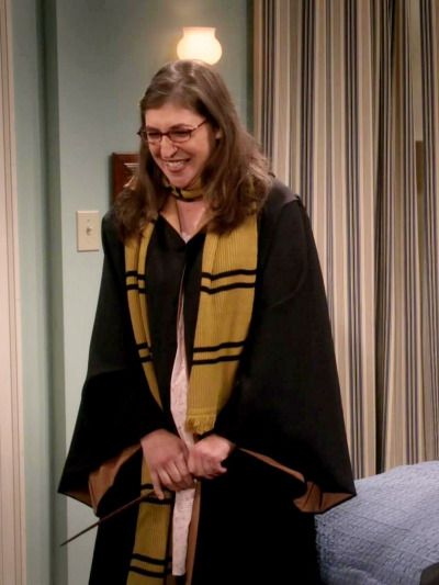 a woman in a black and yellow robe is holding a wand while standing next to a bed