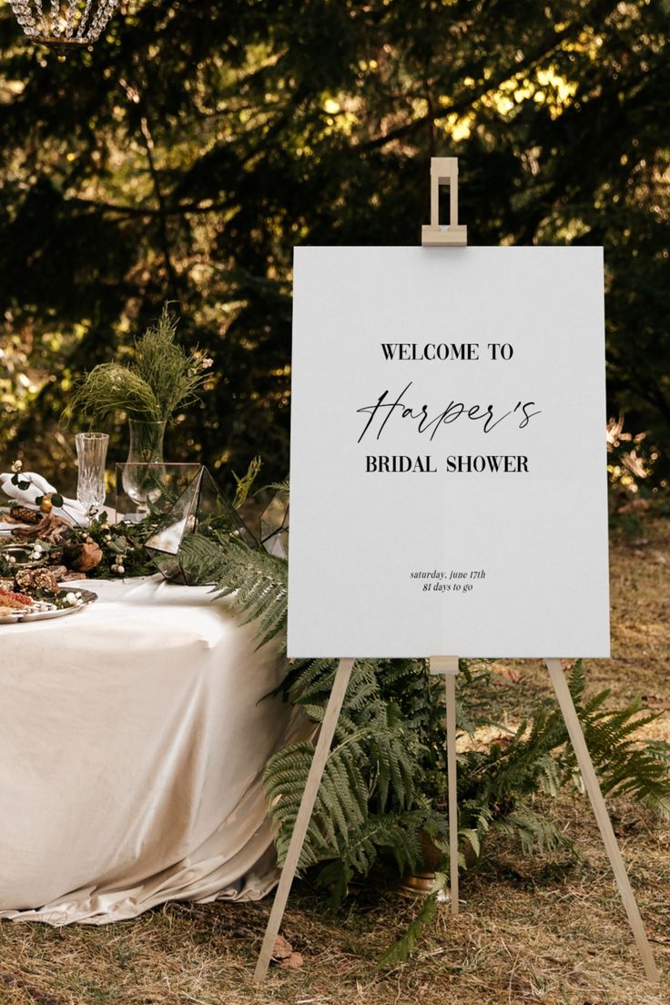 a sign that is on top of a table with flowers and greenery in front of it