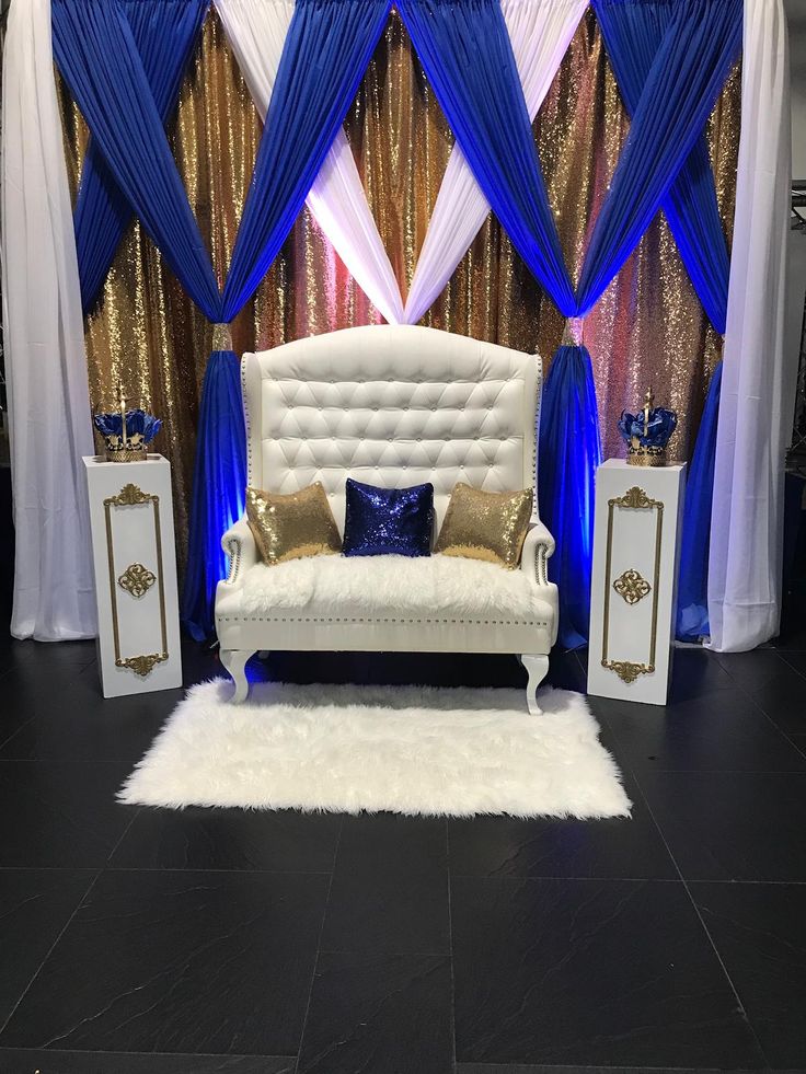 a white couch sitting in front of a blue and gold curtained wall with pillows on it