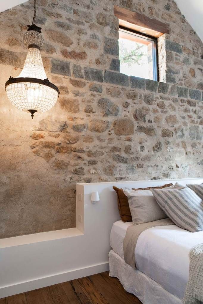 a bed sitting under a window next to a stone wall with a light hanging above it