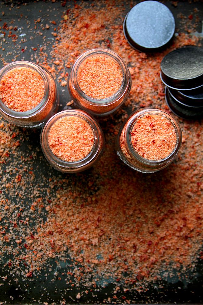 four jars filled with different types of spices on top of a table next to some spoons