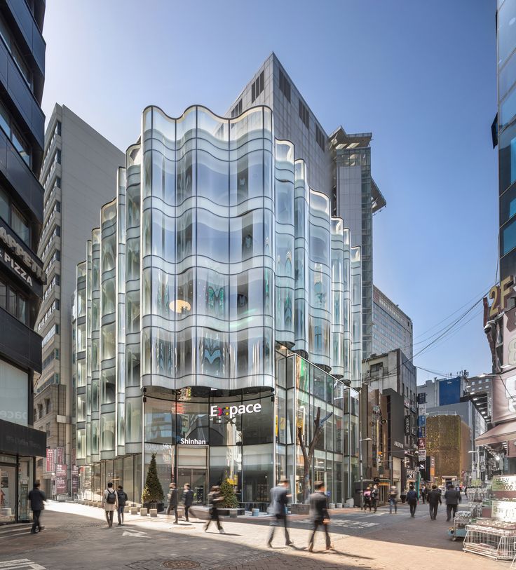 people are walking in front of a glass building on the corner of a city street