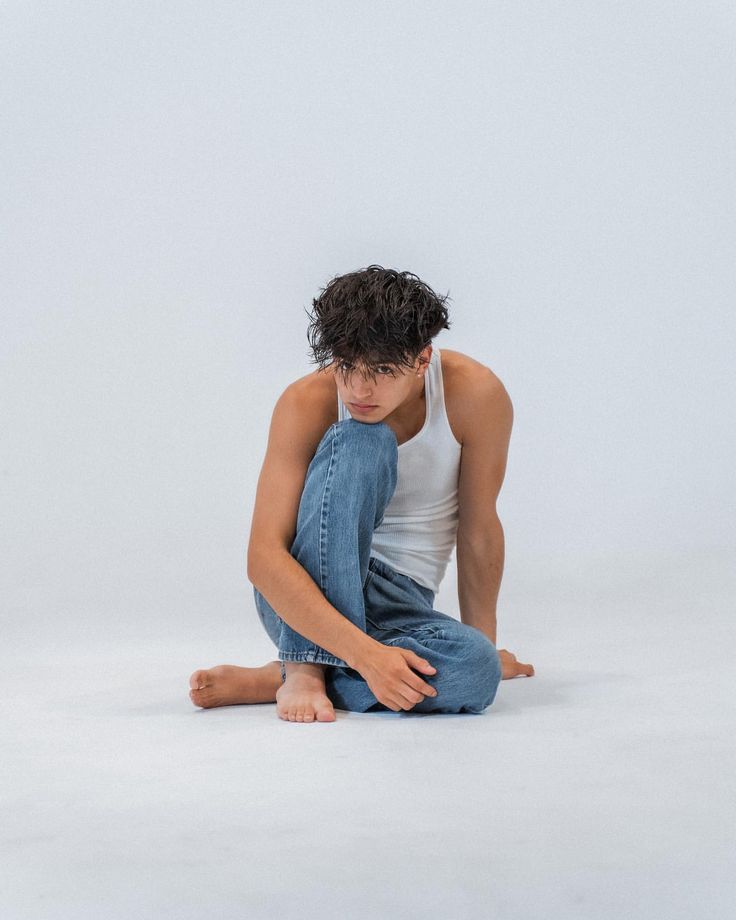 a young man sitting on the floor with his legs crossed and looking down at something