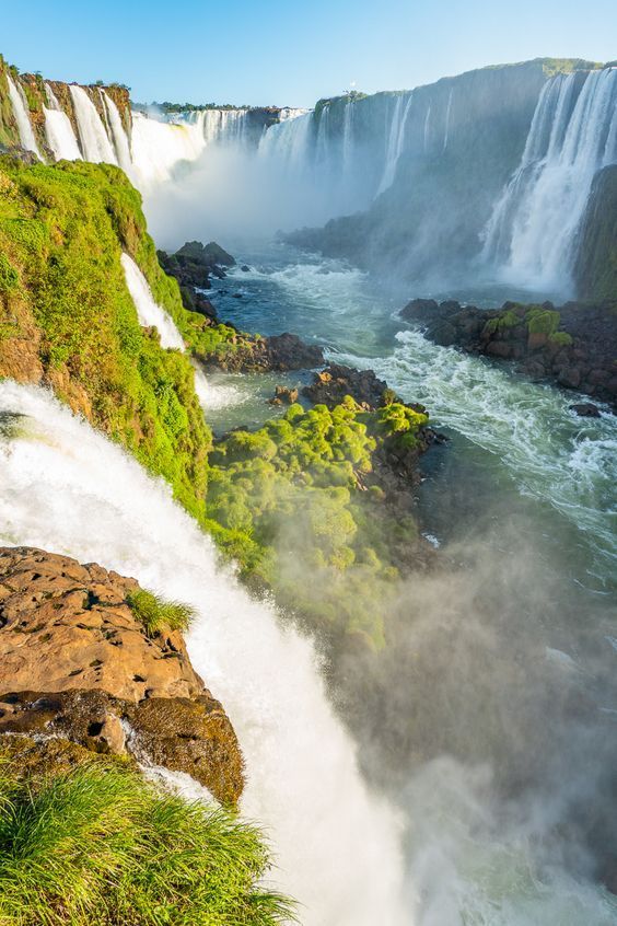 iguana falls in the background with mist coming out from the water and green plants growing on the rocks