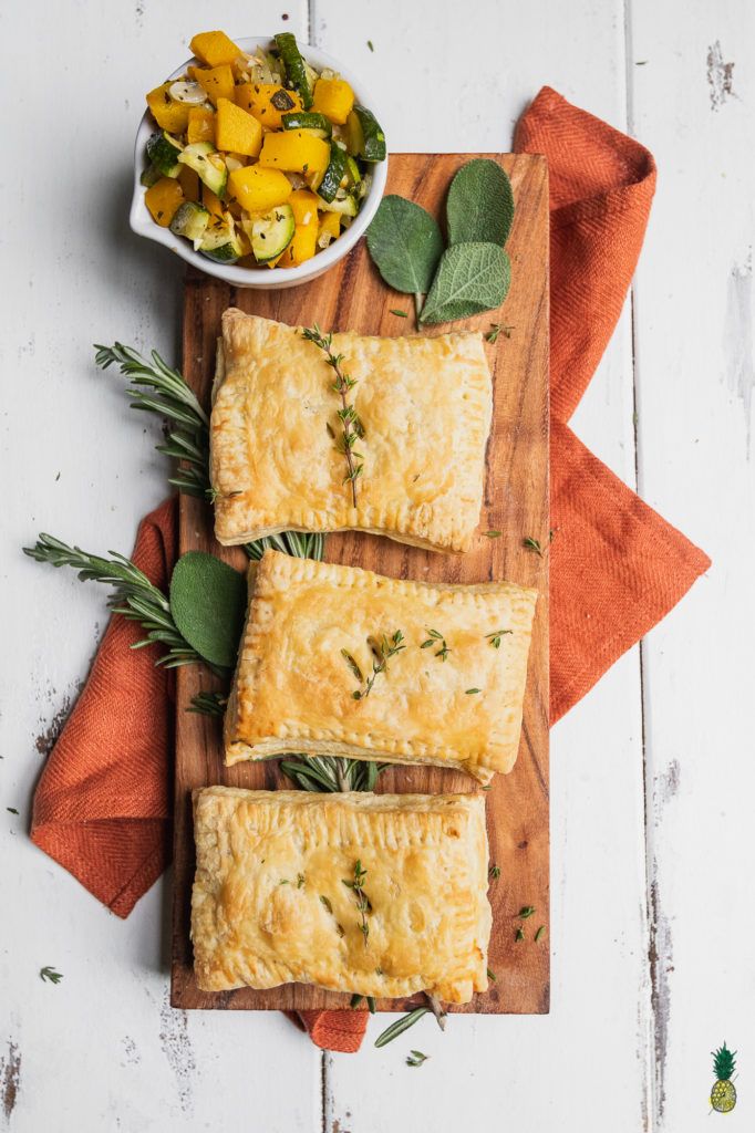 three puff pastries on a cutting board with herbs and sage leaves next to them