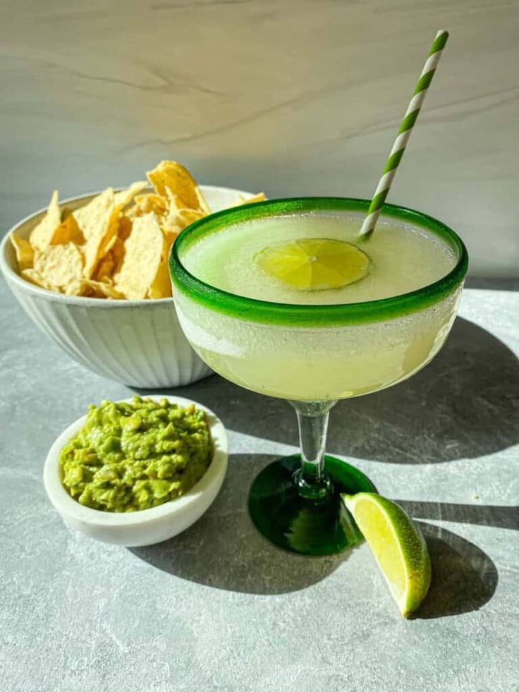 a margarita with a lime wedge and guacamole in a bowl next to it