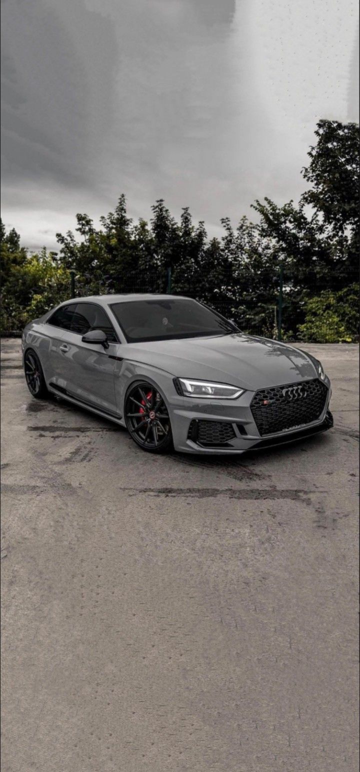 a grey car is parked in a parking lot with trees and dark clouds behind it