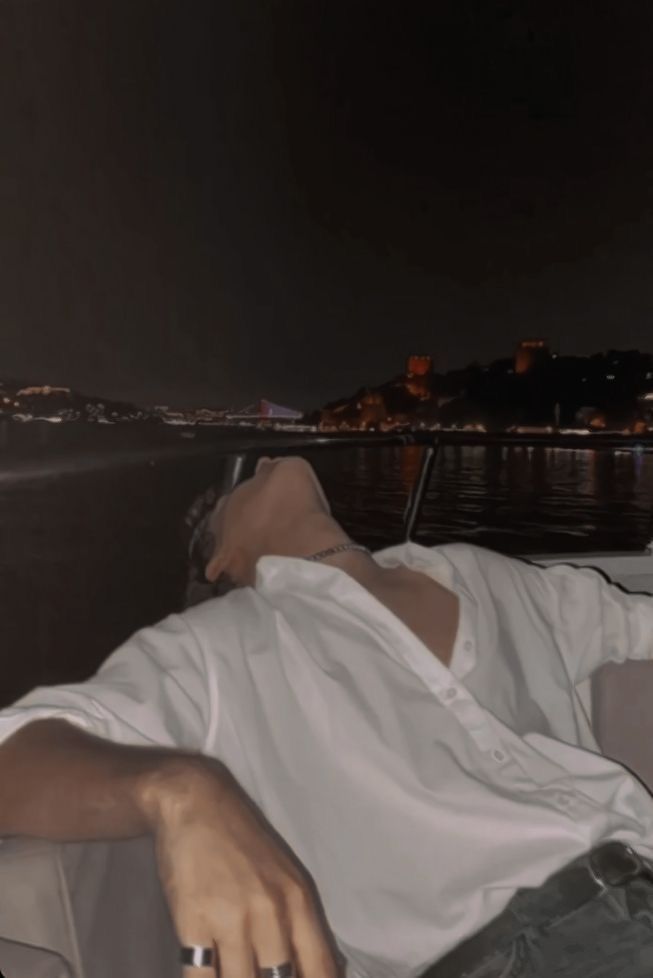 a man laying on top of a couch next to a body of water at night