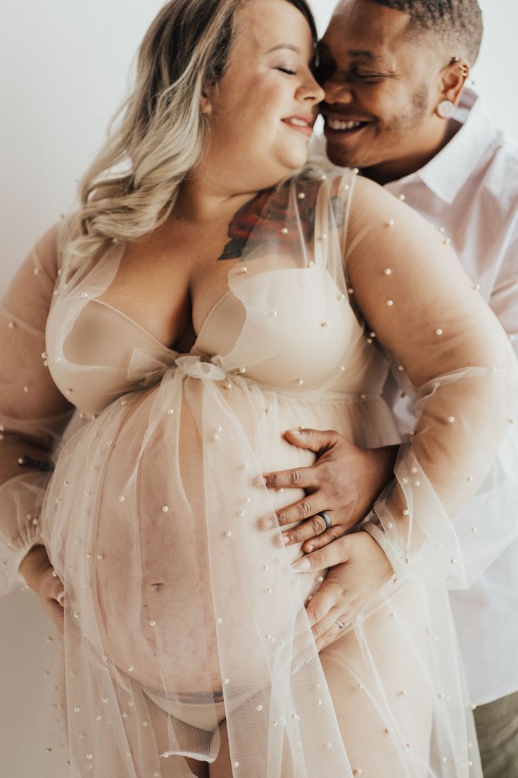 a pregnant woman is hugging her husband's belly while they are dressed in sheer tulle