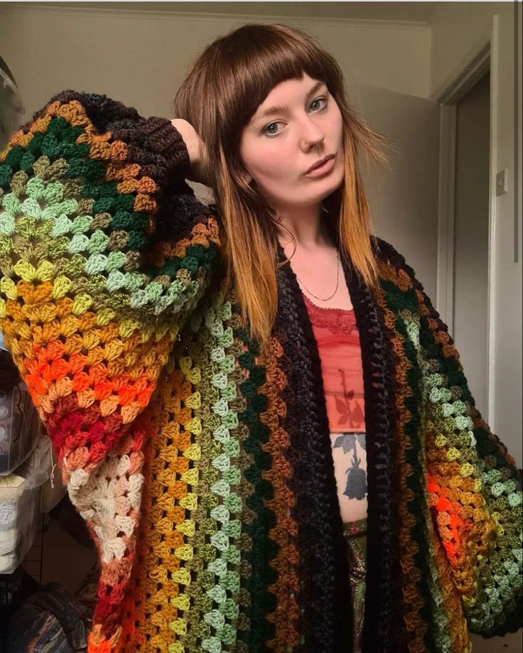 a woman wearing a multicolored crocheted sweater and cardigan standing in front of a door