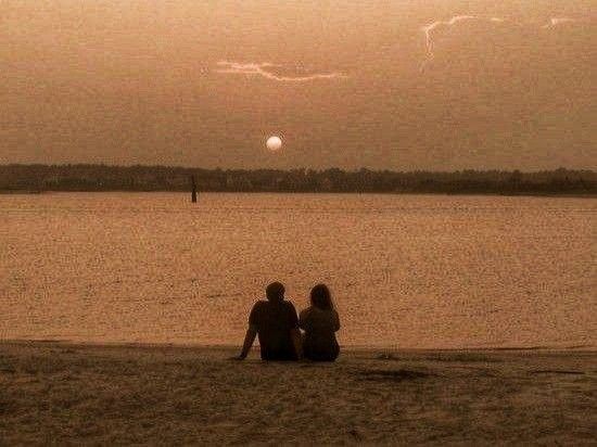 two people sitting on the beach watching the sun set