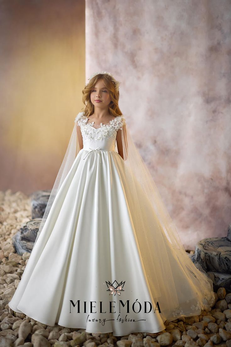 The Pearl Mirage flower girl and First Communion dress exudes sophisticated grace and timeless elegance. The fitted bodice, intricately adorned with hand-stitched lace appliqués and delicate pearl accents, beautifully complements the illusion neckline for a refined yet ethereal look. A removable sparkle cape, shimmering with cascading rows of jewels, adds a touch of regal glamour, perfect for making a memorable entrance. Crafted from the finest European lace, satin, and tulle fabrics, this floor-length, full-circle, multilayered princess skirt glides with elegance, enhanced by a graceful long train. The Pearl Mirage captures the essence of couture luxury, featuring a secure zipper and button closure on the back and fully lined for the utmost comfort and protection, making it the ultimate c Tulle Shawl, Princess Dress Fairytale, Sheer Cape, Fairytale Princess, First Communion Dress, Princess Skirt, Communion Dresses, Illusion Neckline, Elegant Skirt