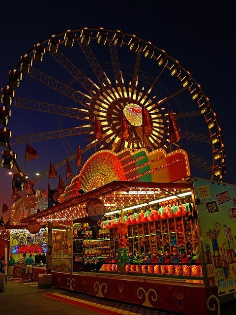 an amusement park ride at night with lights on it's sides and ferris wheel in the background