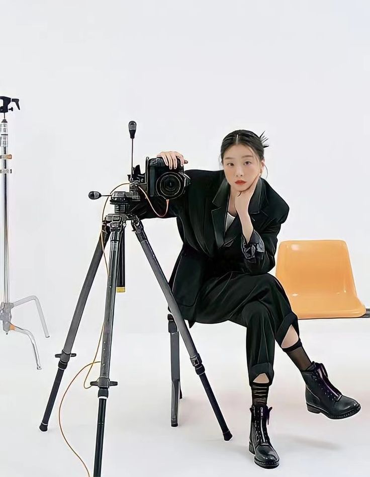 a woman sitting in front of a camera on a tripod with an orange chair behind her