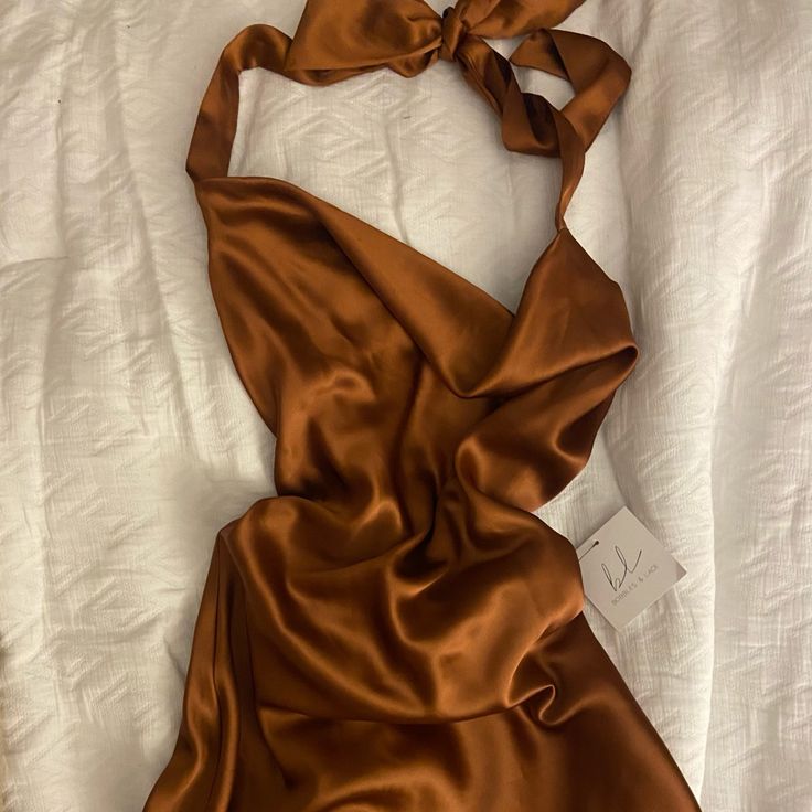 a brown dress laying on top of a bed next to a white sheet with a tag