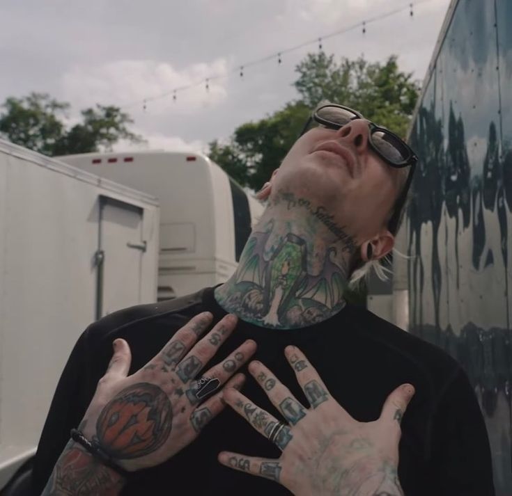 a man with lots of tattoos on his neck and hands standing in front of a trailer