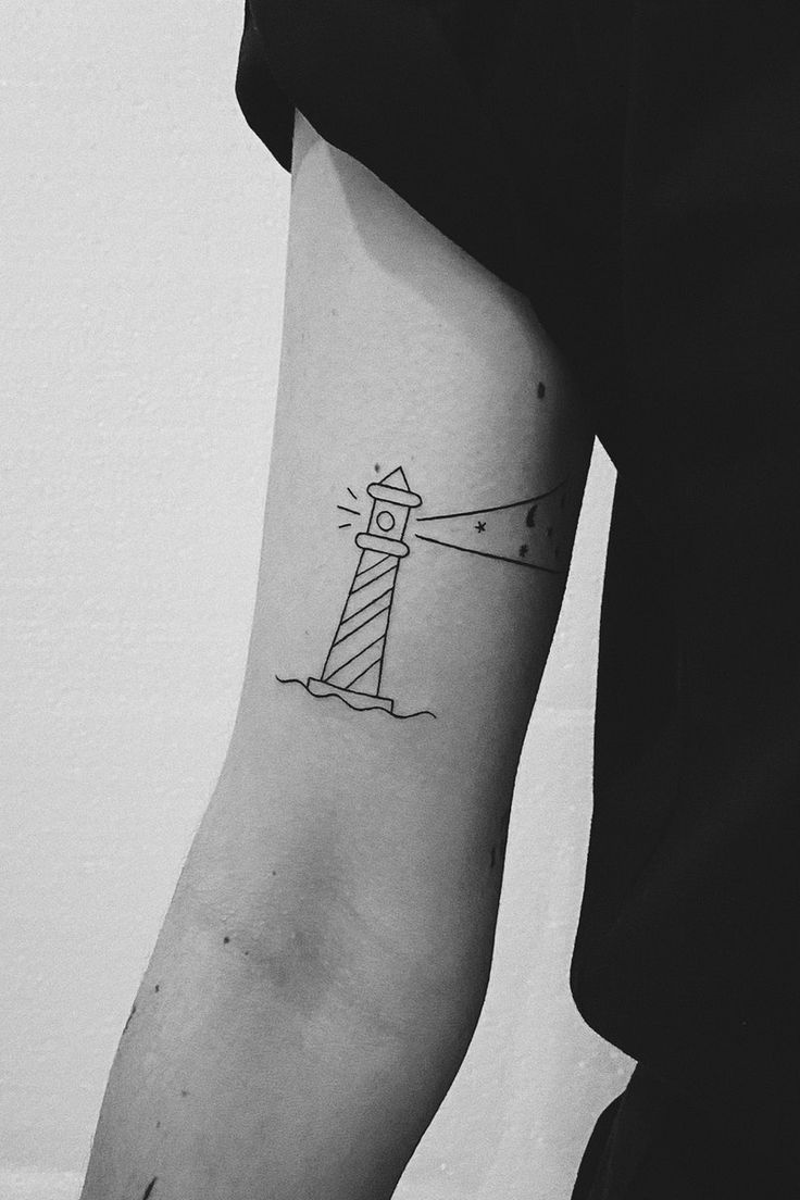 a black and white photo of a person with a lighthouse tattoo on their arm,