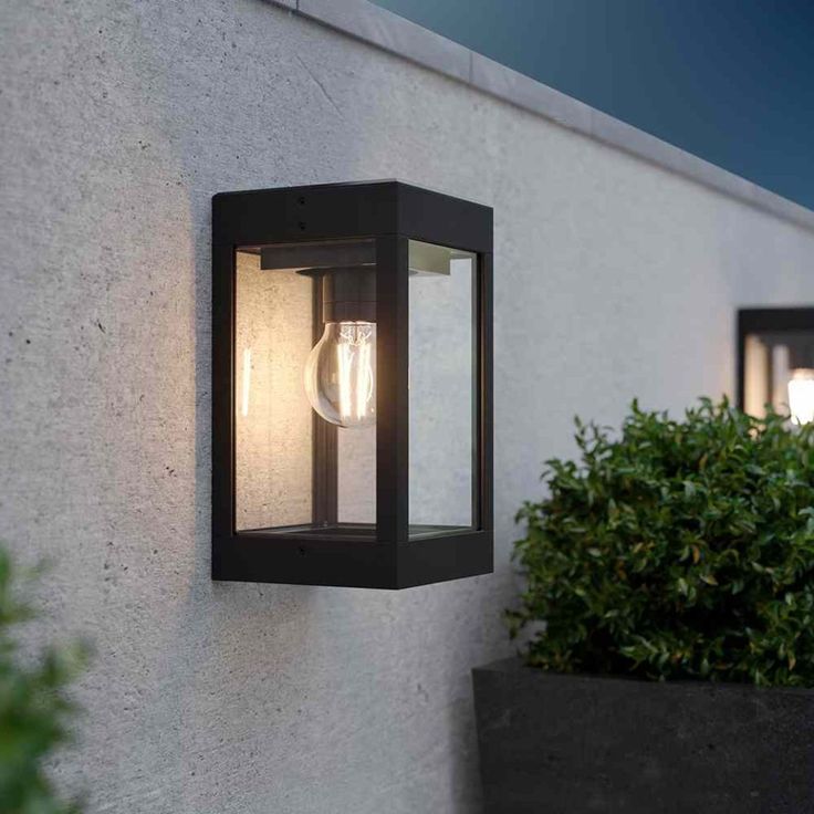 an outdoor light that is on the side of a wall next to a potted plant