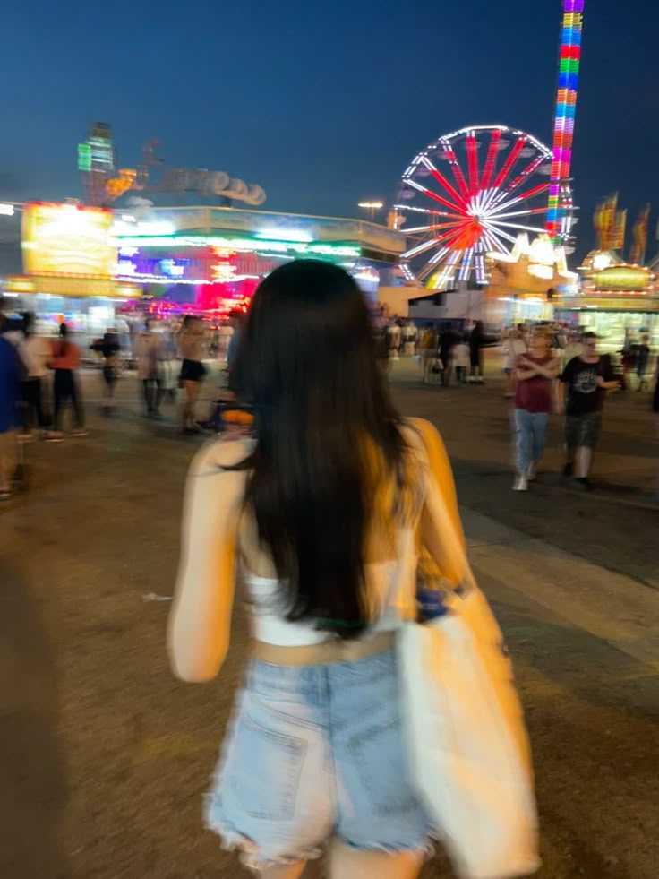 a woman is walking through an amusement park at night