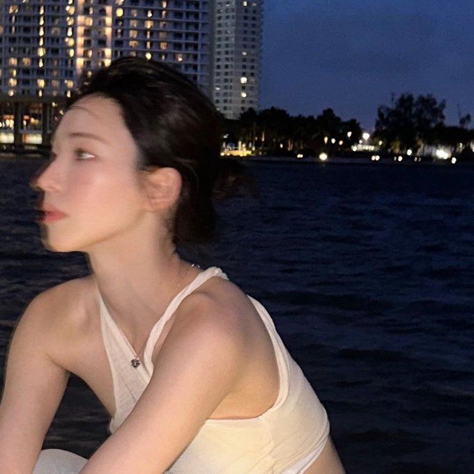 a woman sitting on the edge of a boat in front of a city at night