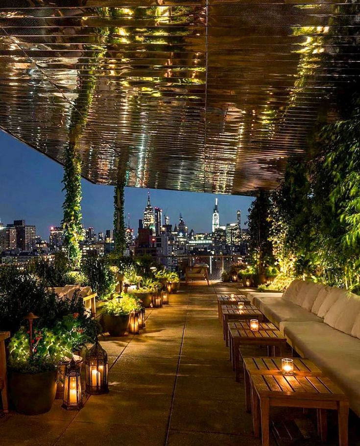 an outdoor seating area with plants and lights on the ceiling is lit up at night