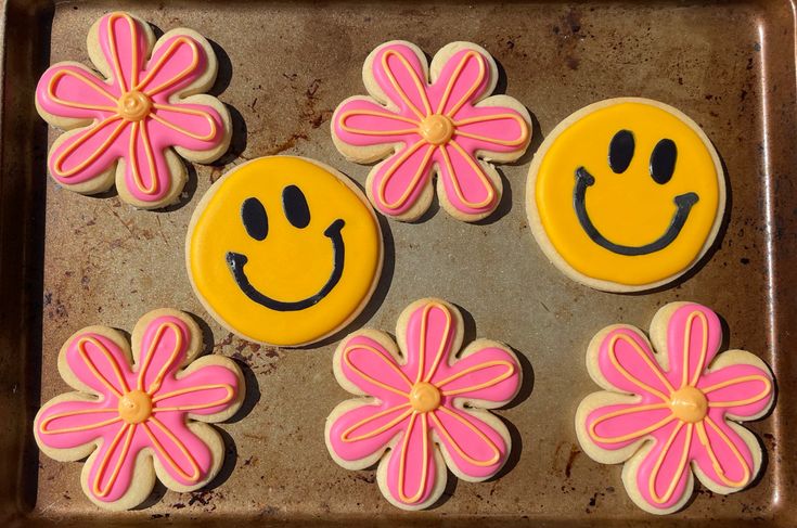 decorated cookies in the shape of smiley face and flowers on a baking sheet with pink icing