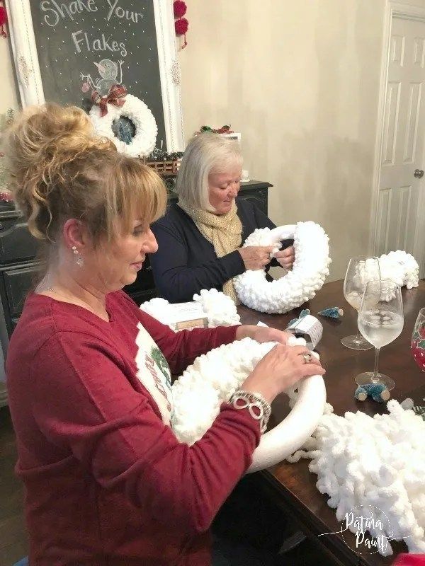 two women sitting at a table making wreaths out of fake snowflakes and wine glasses