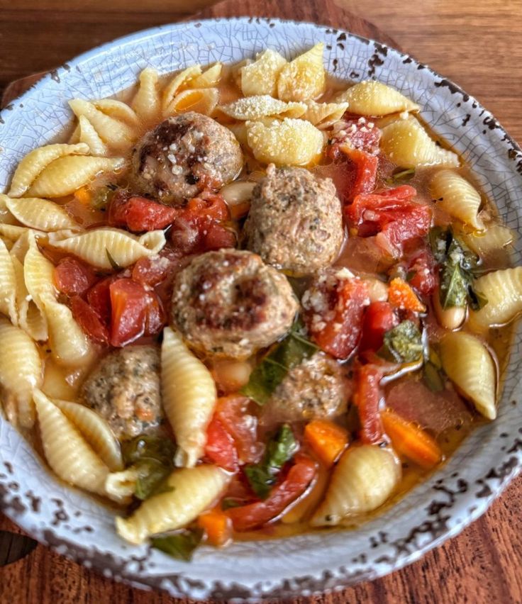 a bowl filled with pasta and meatballs on top of a wooden table next to a fork