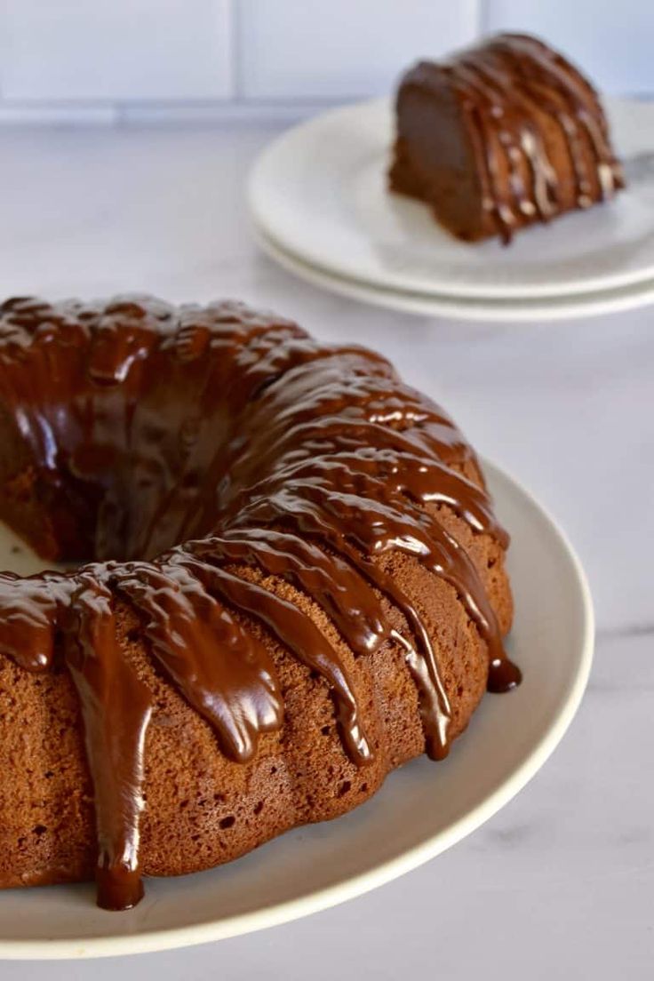 a bundt cake with chocolate icing sitting on a plate next to another bundt cake