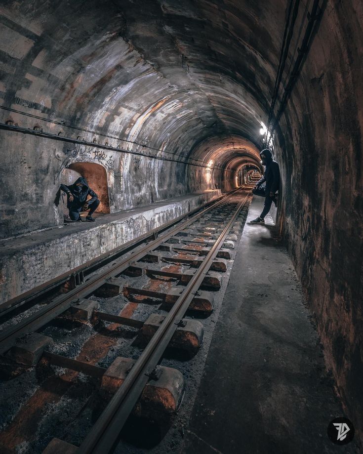 two men are standing in the middle of a tunnel with train tracks running through it