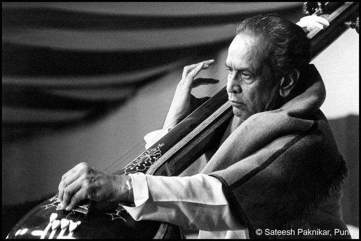 black and white photograph of a man playing the sitar guitar with his hands on his head