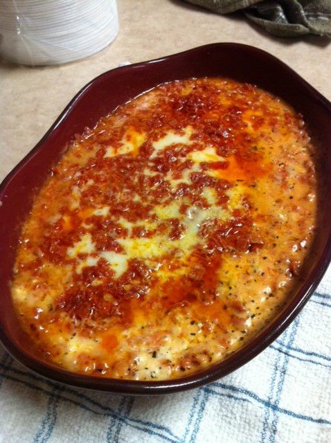 a casserole dish with cheese and sauce in it sitting on a table next to a cup