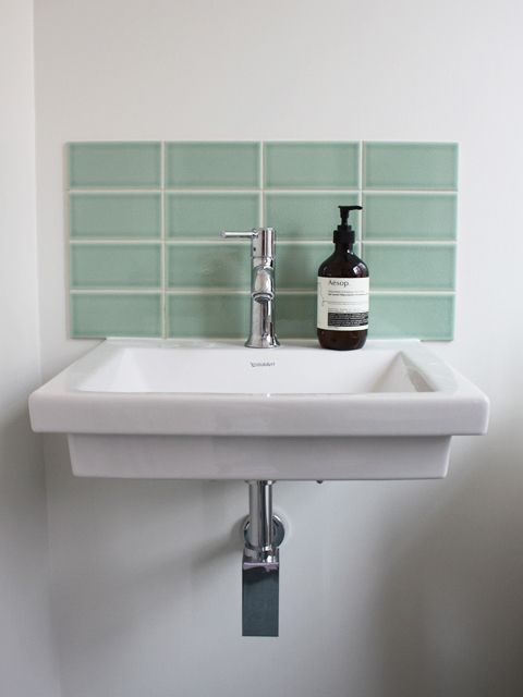 a white sink sitting under a bathroom faucet next to a green tiled wall