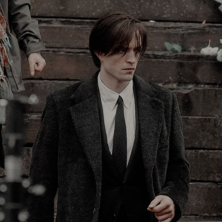 a man in a suit and tie standing next to stairs with other people behind him