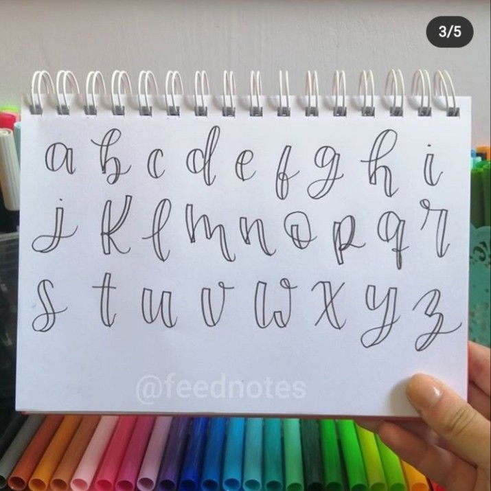 a person holding up a note with the letters drawn on it in front of colored crayons