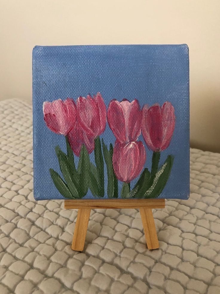 a small easel with pink flowers painted on it sitting on a white bed sheet